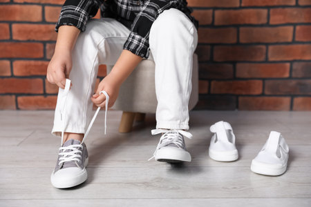 Little girl trying on different shoes near brick wall indoors, closeupの写真素材