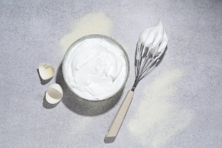 Beating egg whites in bowl, eggshell, flour on gray textured table, flat layの写真素材