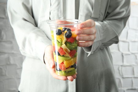 Woman with tasty fruit salad against white brick wall, closeup. Healthy snackの写真素材