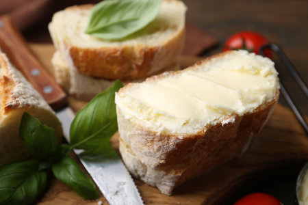 Slices of baguette with butter, basil and knife on wooden table, closeupの写真素材
