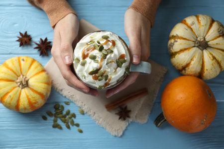 Woman holding tasty pumpkin latte with whipped cream at light blue wooden table, top viewの写真素材