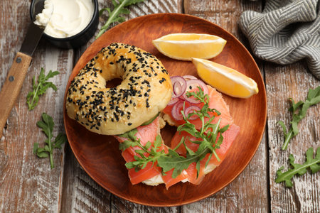 Delicious bagel with salmon, cream cheese, onion, arugula and lemon on wooden table, flat layの写真素材