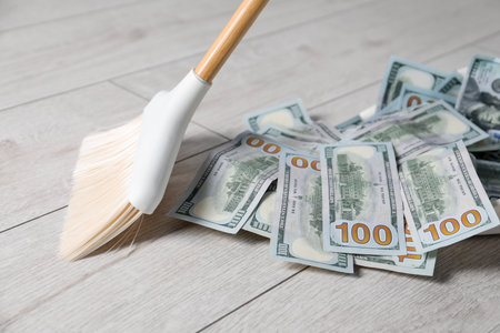 Sweeping dollar banknotes with broom on light wooden floor, closeupの写真素材