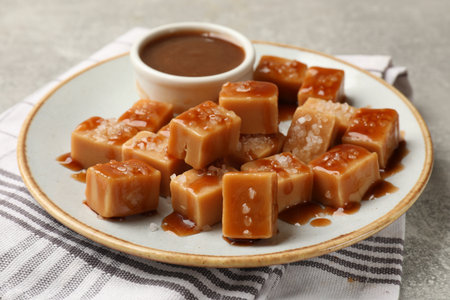 Tasty candies with salt and caramel sauce on gray textured table, closeupの写真素材