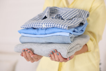 Woman with stack of clothes indoors, closeupの写真素材