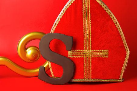 Saint Nicholas (Sinterklaas) day. Miter, crosier and chocolate letter S on red background, closeupの写真素材