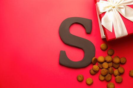 Saint Nicholas (Sinterklaas) day. Chocolate letter S, kruidnoten cookies and gift box on red background, flat lay. Space for textの写真素材