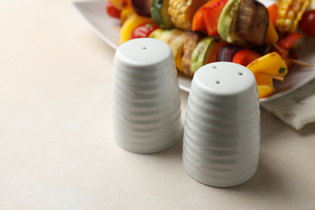 Salt, pepper shakers and tasty grilled vegetables on beige table, closeup. Space for textの写真素材