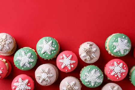 Beautifully decorated Christmas macarons on red background, flat lay. Space for textの写真素材