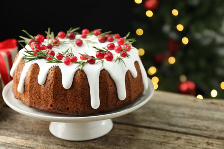 Delicious Christmas cake with icing, cranberries and rosemary on wooden table against black...