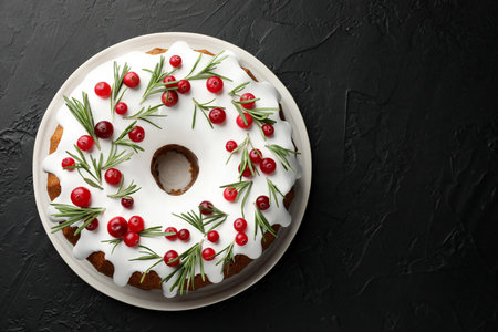 Tasty Christmas cake with icing, cranberries and rosemary on black table, top view. Space for textの写真素材