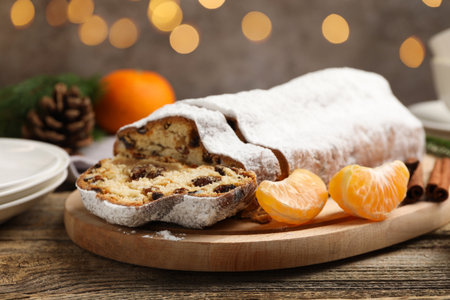 Traditional Christmas Stollen with icing sugar, spices, tangerine and festive decor on wooden table, closeup. Bokeh effectの写真素材