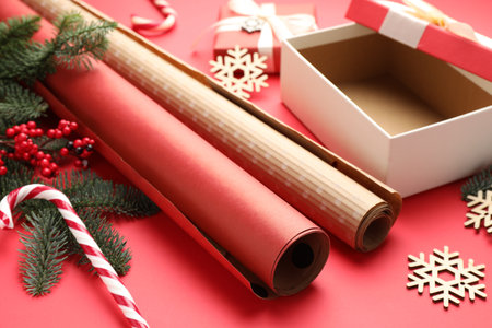 Festive packaging. Gift box, ribbon, wrapping paper and Christmas decor on red background, closeupの写真素材