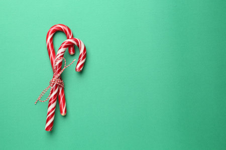 Tasty candy canes with twine on green background, top view with space for text. Merry Christmas and...