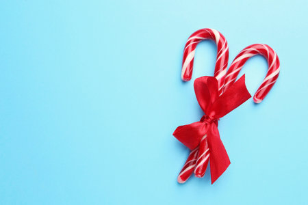 Tasty candy canes with bow on light blue background, top view with space for text. Merry Christmas and Happy New Yearの写真素材