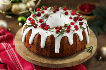 Delicious Christmas cake with icing, cranberries and rosemary on wooden table, closeupの写真素材