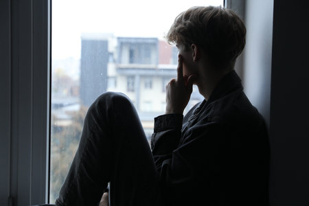 Depressed teenage boy near window at homeの写真素材
