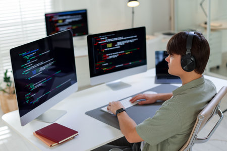 Programmer in headphones working on computer at white table in office
