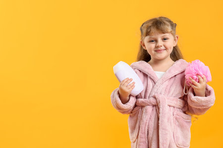 Happy girl in bathrobe with loofah and cosmetic product on yellow background. Space for textの写真素材