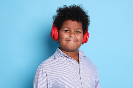 Cute little boy in headphones on light blue background
