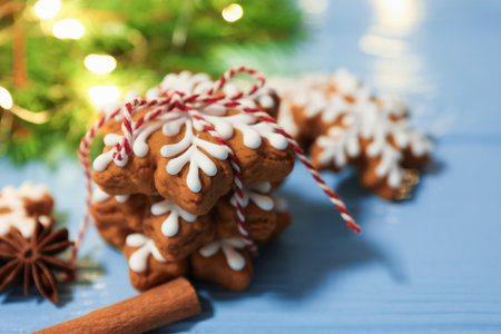 Tasty gingerbread cookies, spices and fir tree branches with lights on blue wooden background, closeup. Christmas treatの写真素材