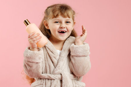 Cute girl in bathrobe with cosmetic product on pink backgroundの写真素材