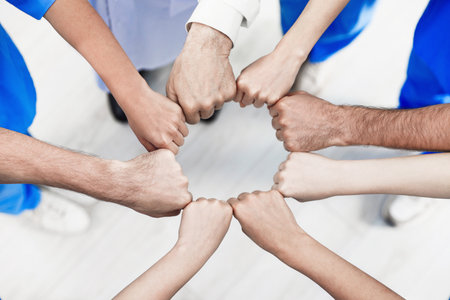 Doctor and interns holding fists together indoors, above viewの写真素材