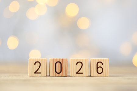 New 2026 year. Cubes with numbers on wooden table against blurred festive lightsの写真素材