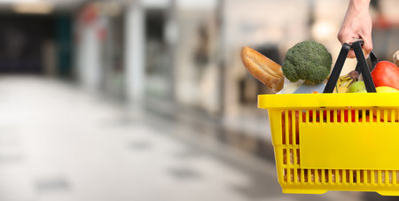 Customer holding shopping basket with different food products at supermarket, closeup. Banner designの写真素材