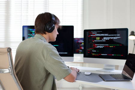 Programmer in headphones working on computer at white table in officeの写真素材