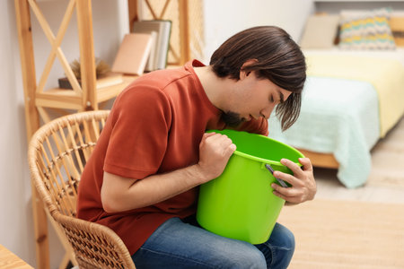 Man with bucket suffering from nausea at homeの写真素材
