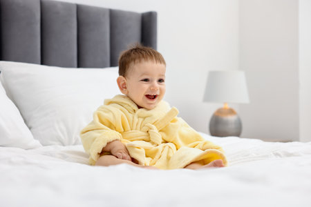Cute baby in bathrobe on bed at homeの写真素材