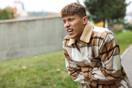 Young man suffering from stomachache and nausea outdoors. Space for text