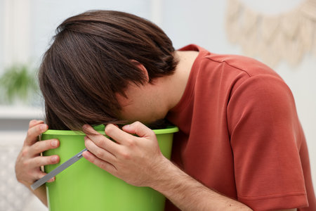 Man with bucket suffering from nausea at homeの写真素材