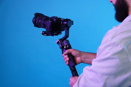 Videographer using gimbal stabilizer with camera on light blue background, closeup
