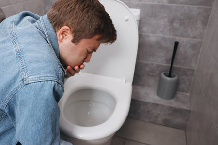 Young man suffering from nausea over toilet bowl in bathroomの写真素材