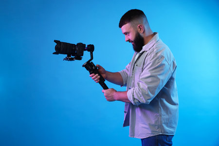 Videographer using gimbal stabilizer with camera on light blue backgroundの写真素材