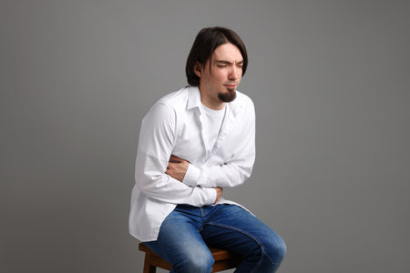 Man suffering from stomach ache and nausea on gray backgroundの写真素材