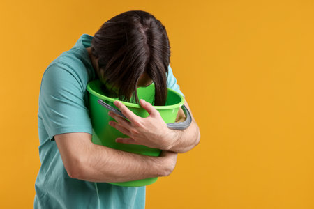 Man with bucket suffering from nausea on yellow background. Space for textの写真素材