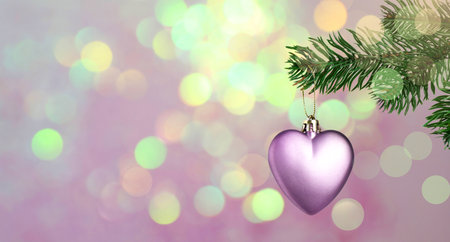 Christmas ornament in shape of heart hanging from fir tree branch against blurred lights on pink background, bokeh effect. Banner designの写真素材