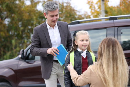 Parents taking their daughters to school near car outdoors