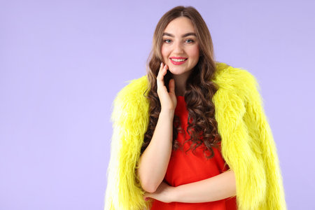 Beautiful woman in fur coat posing on violet background, space for textの写真素材