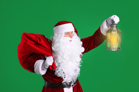 Santa Claus with red bag of Christmas gifts and lantern on green backgroundの写真素材