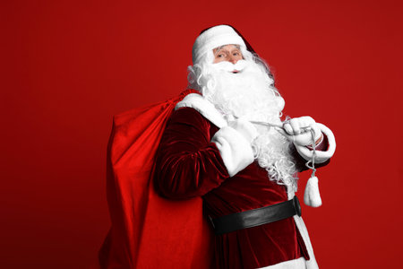 Santa Claus with bag of Christmas gifts on red backgroundの写真素材