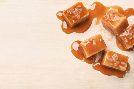 Tasty candies, salt and caramel sauce on light wooden table, flat lay. Space for textの写真素材