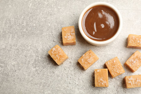 Tasty candies with salt and caramel sauce on gray textured table, flat lay. Space for textの写真素材