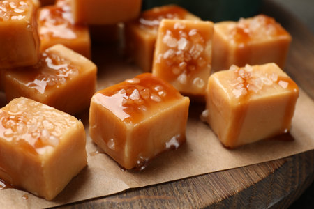 Tasty candies with salt and caramel sauce on wooden board, closeupの写真素材