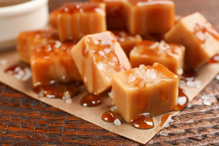 Tasty candies with salt and caramel sauce on wooden table, closeupの写真素材