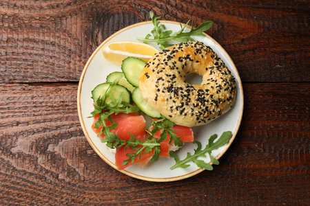 Delicious bagel with salmon, cucumber, arugula and lemon on wooden table, top viewの写真素材