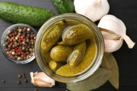 Pickled cucumbers in jar, fresh vegetables and spices on black wooden table, flat layの写真素材